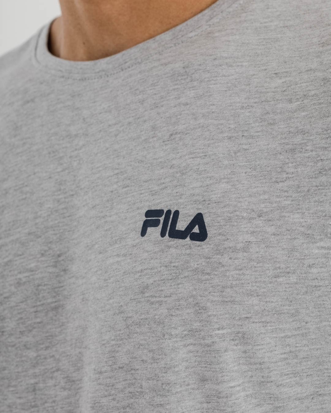 close up of man wearing grey t-shirt with Fila logo on top left